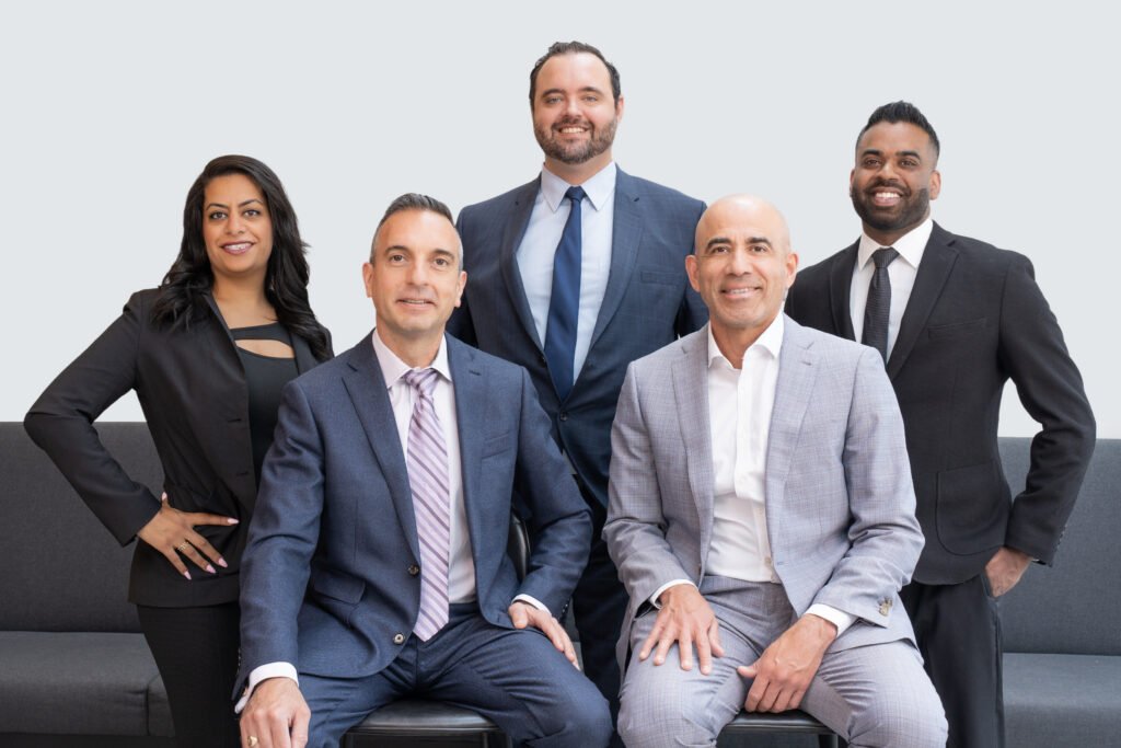 Group of five professionals in suits posing together on a sofa, smiling at the camera (team photo).